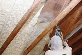 Spray foam insulation being applied to white pipes in a wall.