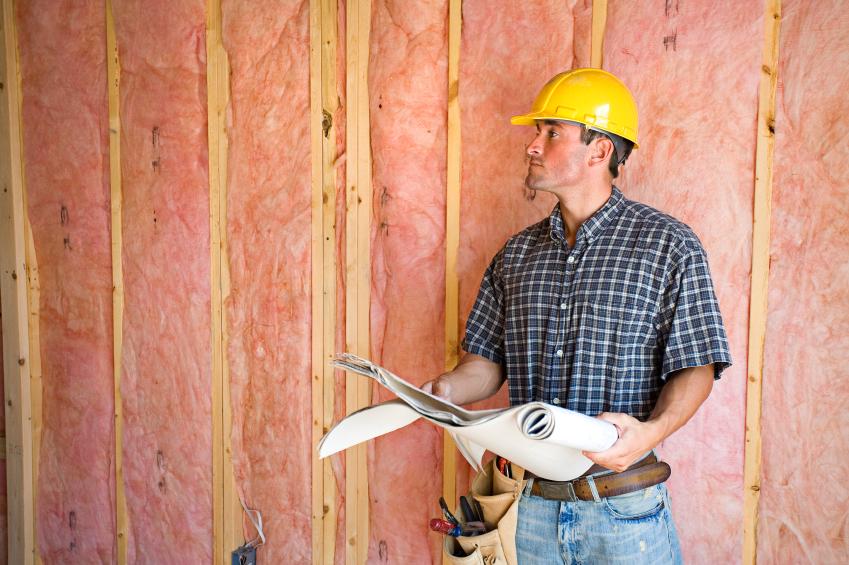 Man with construction hat standing next to open wall with newly installed fiberglass insulation