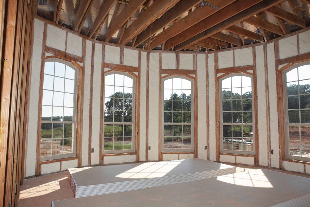 Spray foam insulation installed in a home's walls, around a curved wall of tall windows.